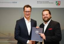 NRWs Verkehrsminister Wüst (l.) übergibt Christian Betchen von der KWS den Förderbescheid