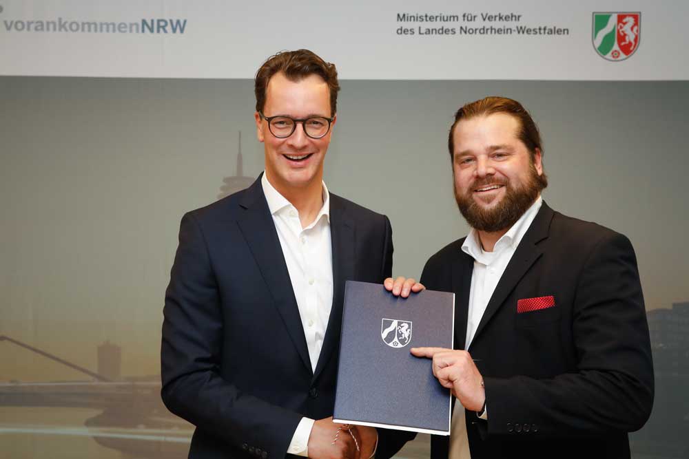 NRWs Verkehrsminister Wüst (l.) übergibt Christian Betchen von der KWS den Förderbescheid